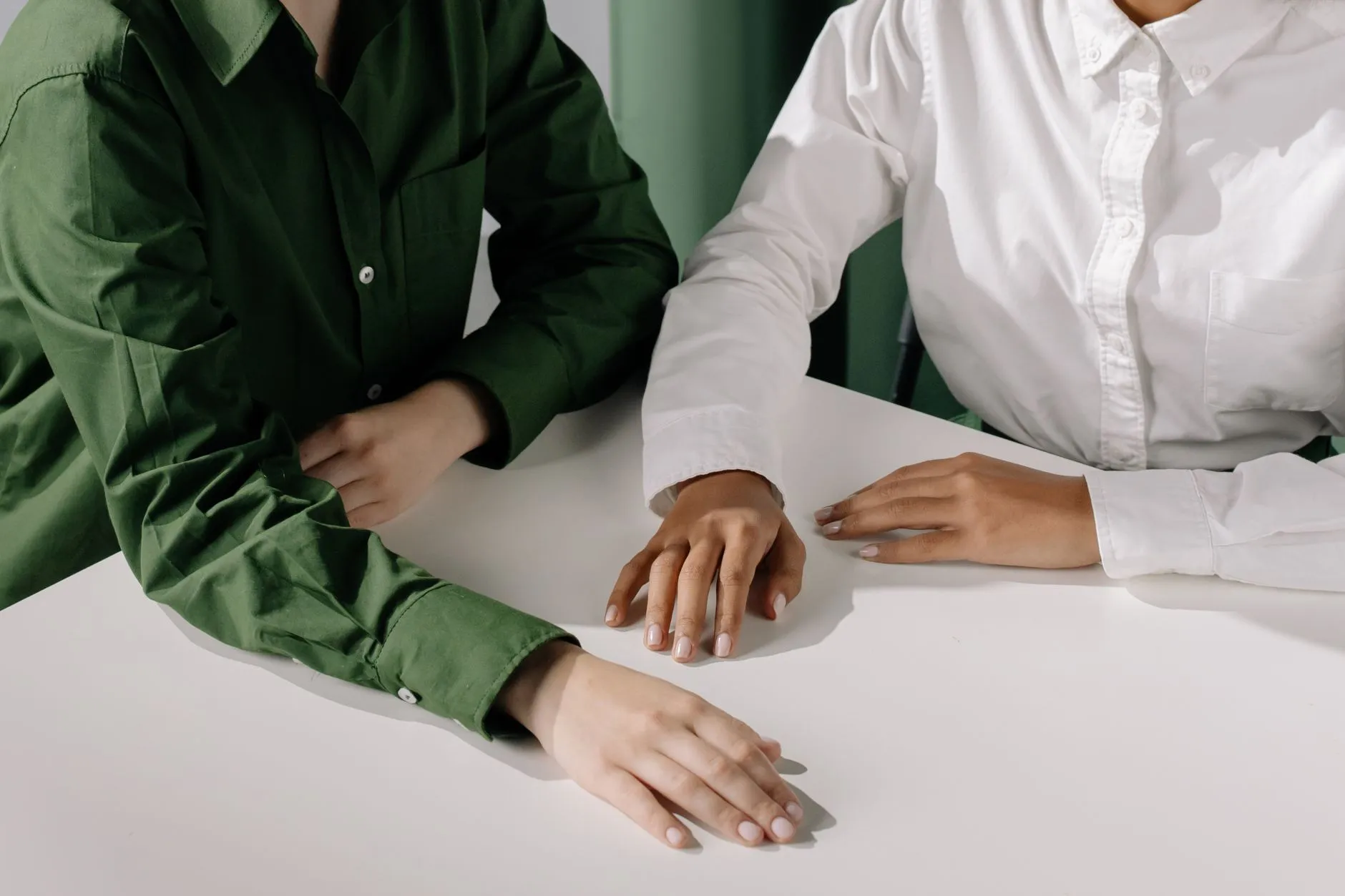 Two people side by side at a white table, hands resting on it, mid-conversation