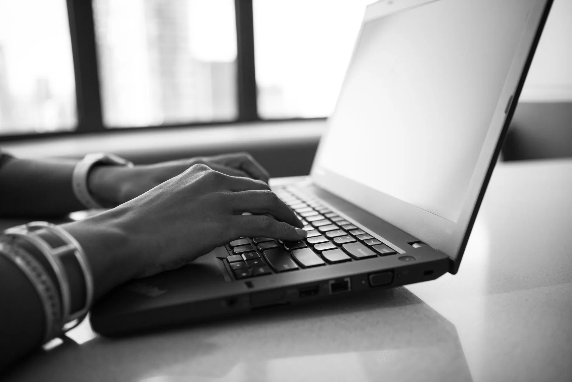 Hands at a laptop keyboard by a bright window